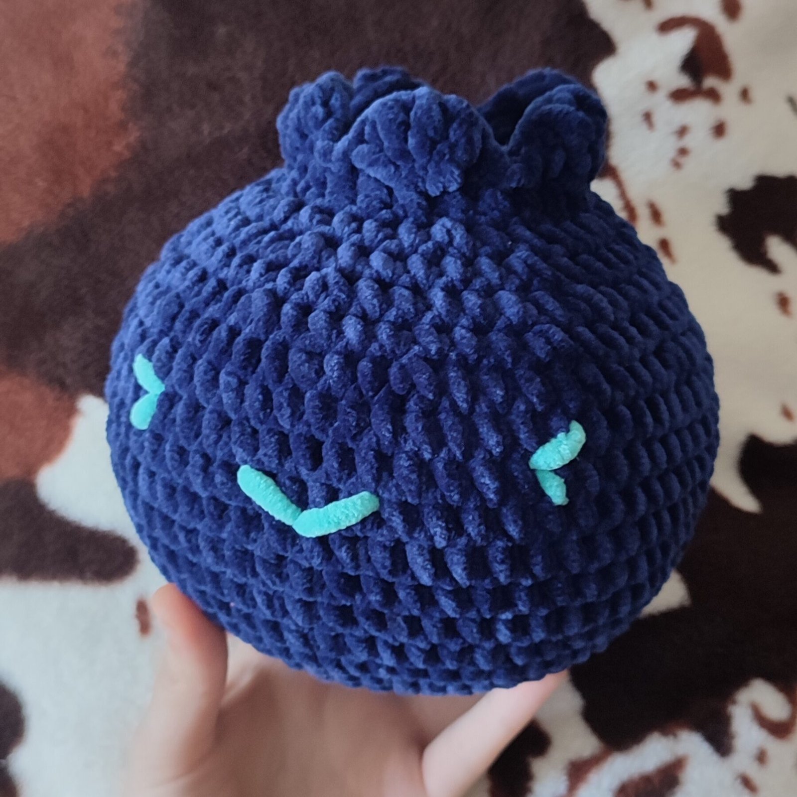 Blueberry plush in a hand. The photo is taken in a more realistic home setting, in front of a blanket.