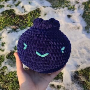 Blueberry plush in a hand. The photo is taken in front of greenery covered in snow.