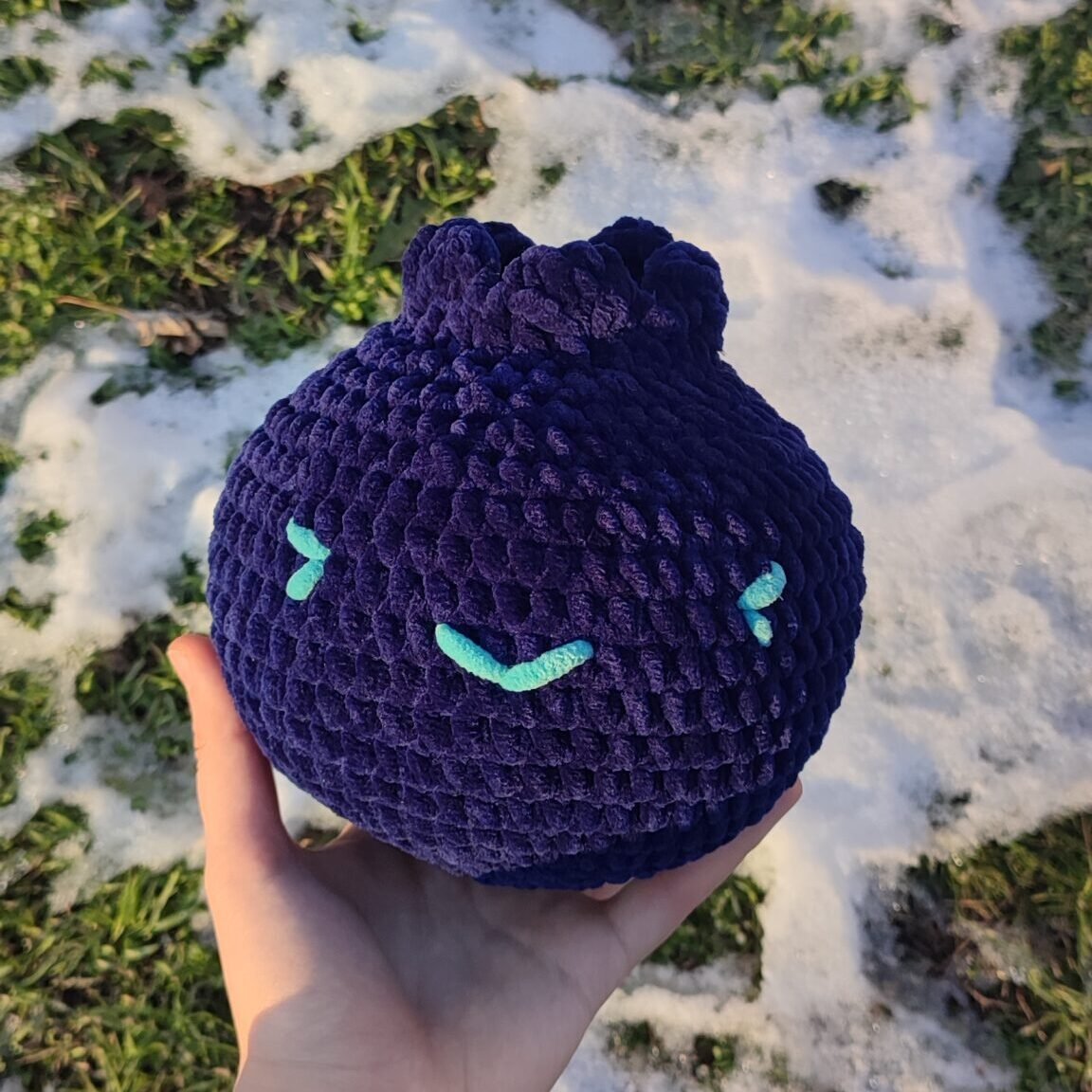 Blueberry plush in a hand. The photo is taken in front of greenery covered in snow.