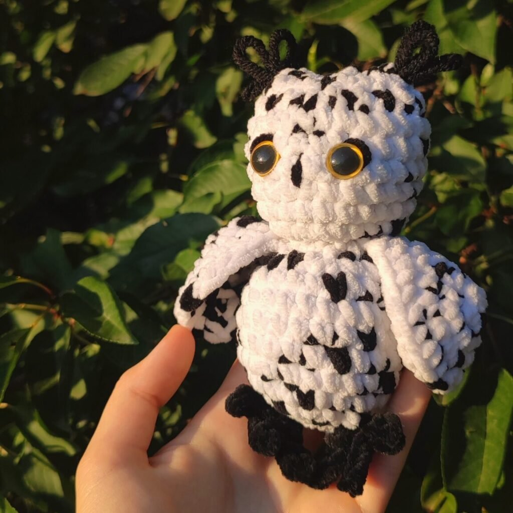 Snowy owl keychain in a hand. Photo taken under direct sunlight in front of some greenery.