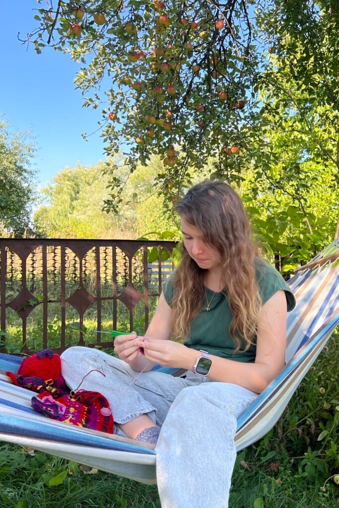 A crochet pattern designer focused on a vibrant yarn project, sitting cross-legged in an outdoor hammock.